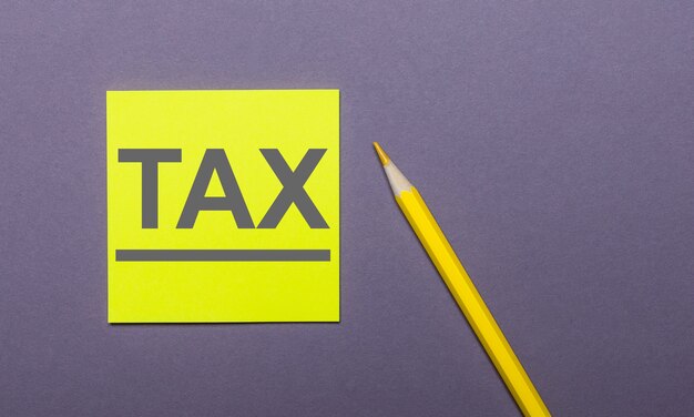 On a gray background, a bright yellow pencil and a yellow sticker with the word TAX