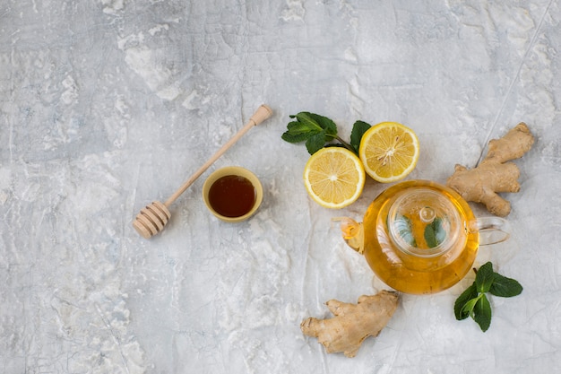 on a gray background herbal tea in a transparent teapot, ginger, lemon, honey and mint