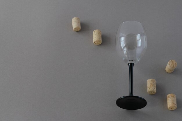 On a gray background, one empty glass wine goblet with scattered corks. The photo is horizontal.