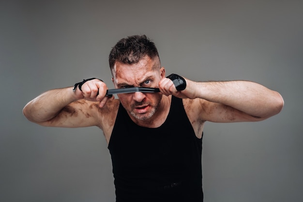 On a gray background stands a battered man in a black T shirt looking like a fighter and preparing for a fight.