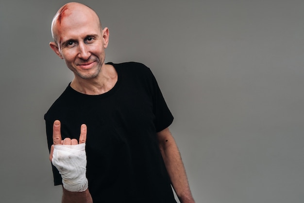 On a gray background stands a battered man in a black T-shirt With his hands wrapped up