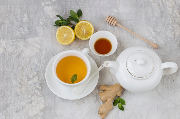 on a gray background teapot, tea with mint in a cup, ginger, lemon, honey and mint