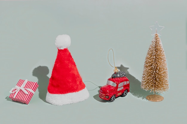 Gray background with Christmas or New Year symbol attribute objects and symbolic items concept. Pink gift box present with ribbon, small red taxi car toy, fir tree and red festive santa hap or cap