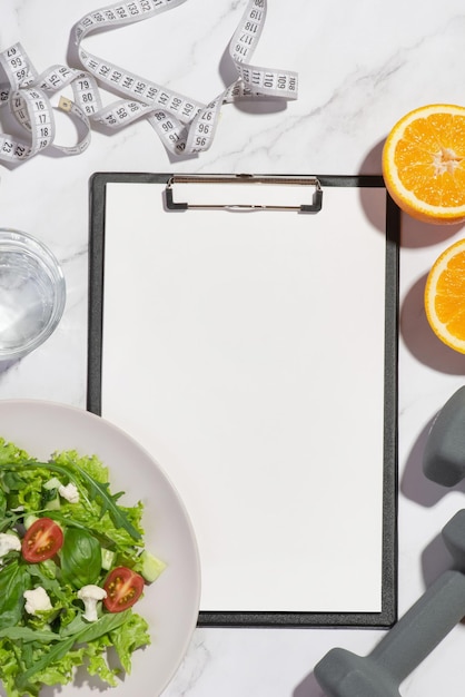 Gray background with tablet lettuce orange dumbbells and measuring tape