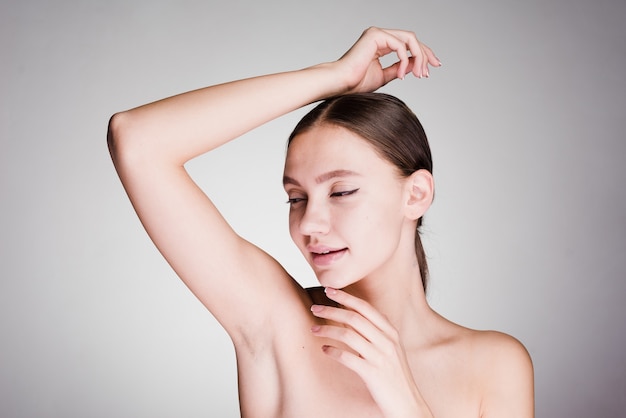 On a gray background a woman after a shower looks after the skin of the armpits