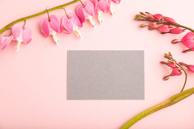 gray business card with pink dicentra, broken heart flowers on pink pastel background. top view