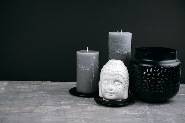 Gray candles and white ceramic Buddha head on a table opposite black wall