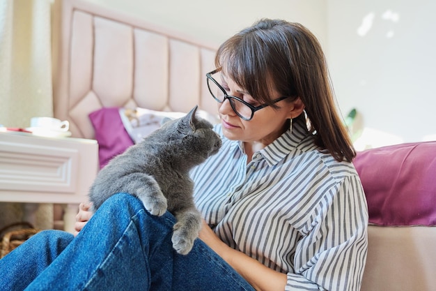 gray cat in hands of woman at home cat sitting on knees woman owner talking touching pet love friendship animals people concept