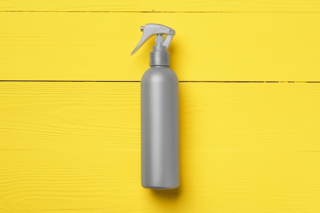 Gray cosmetic bottle on yellow wooden background top view