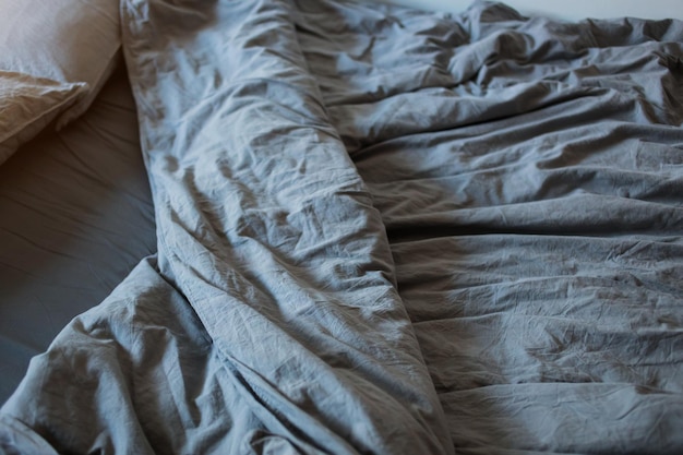 A gray cotton sheet and blankets with pillows on the bed