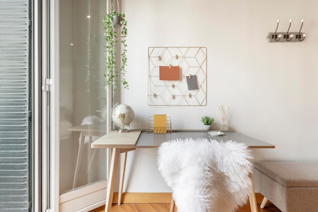 Gray desk with white goatskin chair with coat rack on the wall hanging plant note holders and exit to a terrace