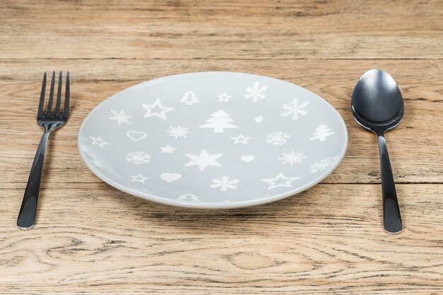 gray empty plate with christmas pictures with cutlery on an old wooden table