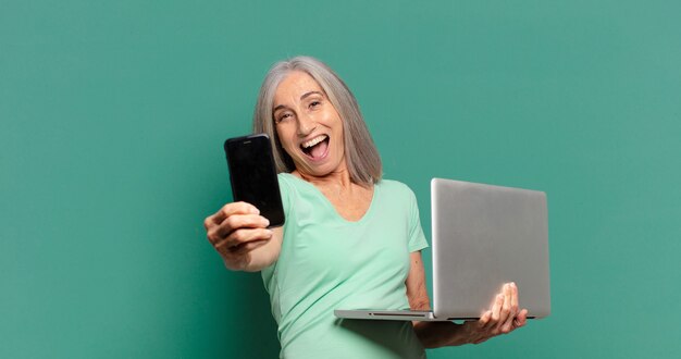 Bella donna con i capelli grigi con un cellulare e un laptop