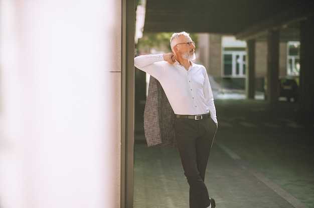 Foto un uomo elegante dai capelli grigi in piedi vicino al muro vicino all'edificio degli uffici