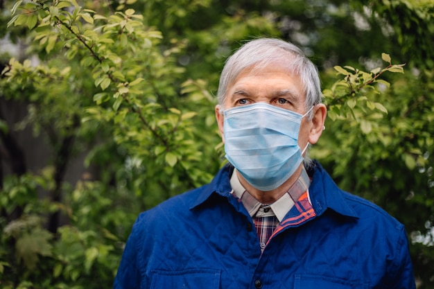 Gray-haired grandfather with covid protection on face. Old man with gray hair in protective medicine mask outdoors.