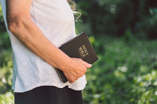 Седая бабушка держит в руках библию.