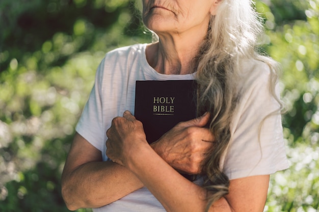 Gray-haired grandmother holds bible in her hands. 