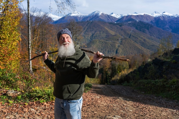 Gray-haired ld man with a beard conquers the summit, concept of tourism and recreation in old age