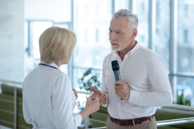 Gray-haired male journalist interviewing blonde female doctor