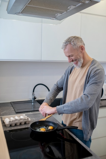 Седовласый мужчина готовит омлет на кухне