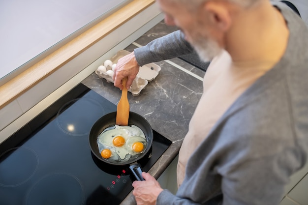 A gray-haired man cooking omlette in the kitchen