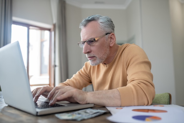 Uomo dai capelli grigi che lavora su un laptop e sembra occupato