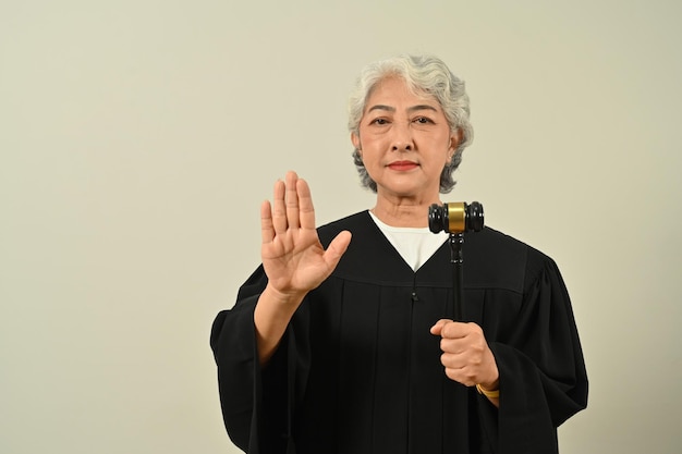 Gray haired senior judge in robe gown uniform holding a gavel in hand and looking to camera Lawyer justice and law attorney