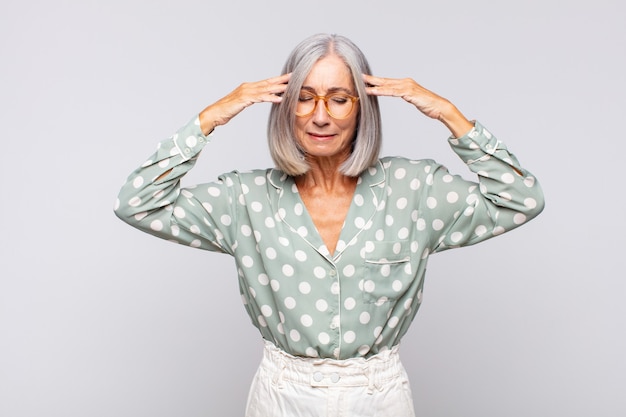 Gray haired woman looking concentrated, thoughtful and inspired, brainstorming and imagining with hands on forehead