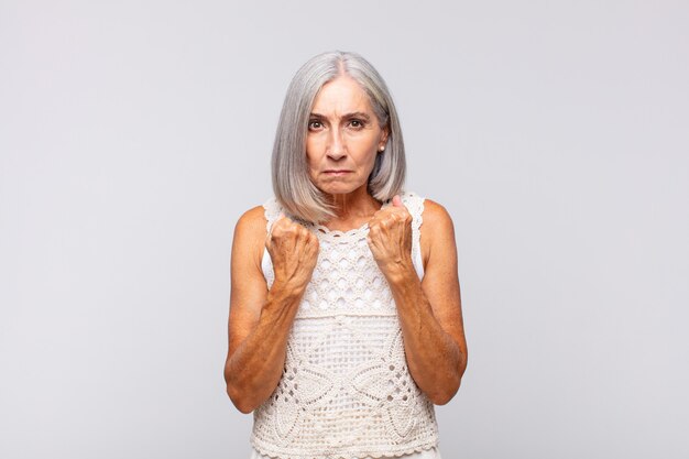 Gray haired woman looking confident, angry, strong and aggressive, with fists ready to fight in boxing position