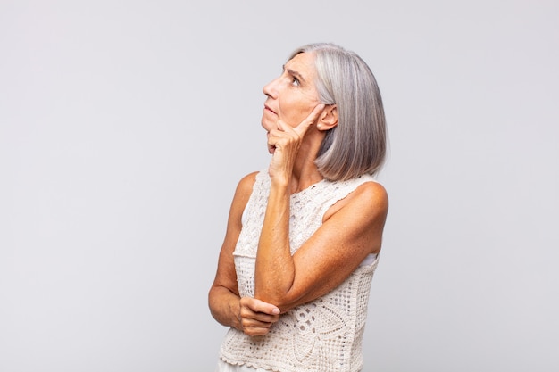 Gray haired woman with a concentrated look, wondering with a doubtful expression, looking up and to the side