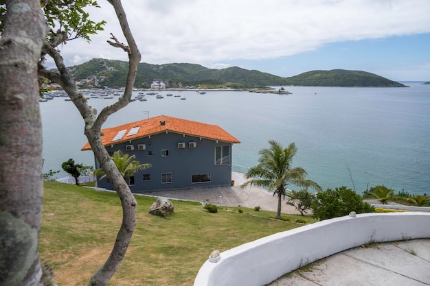 A gray house with a red roof and solar panels on it on the shore of the bay