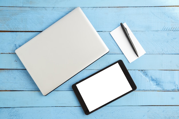 Gray laptop ,black tablet ,small paper notebook and black pen on blue wood