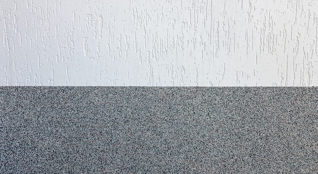 Gray marble chips and decorative light stucco on the wall divided by a horizontal line. Building facade background. Stucco texture on the street.