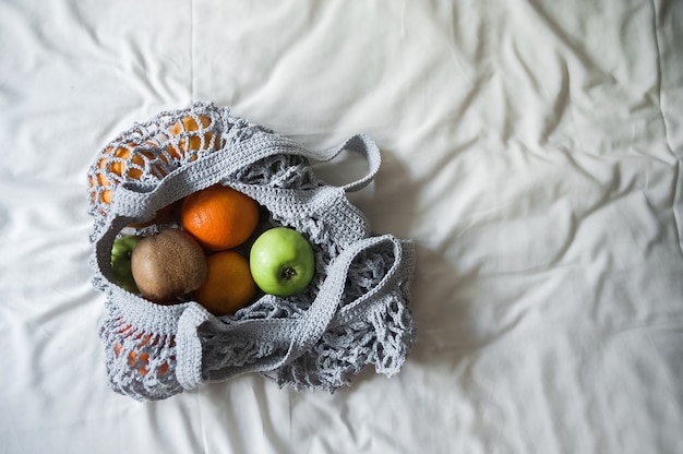 Gray mesh bag with yellow oranges close-up and copy space. Handmade eco bag on textiles