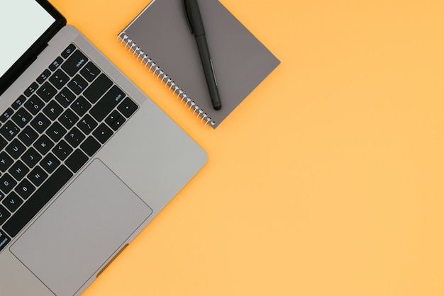 Gray modern laptop and notepad with pen on an orange surface