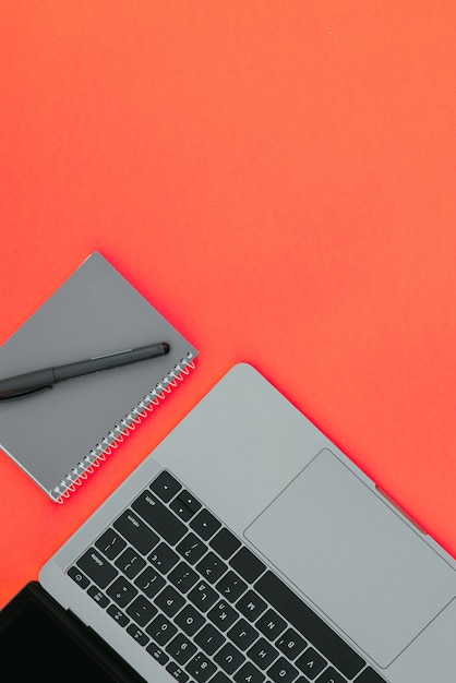 Серый современный ноутбук и блокнот с ручкой на красной поверхности