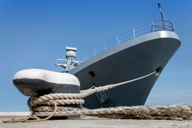 A gray modern warship moored by ropes on the shore.