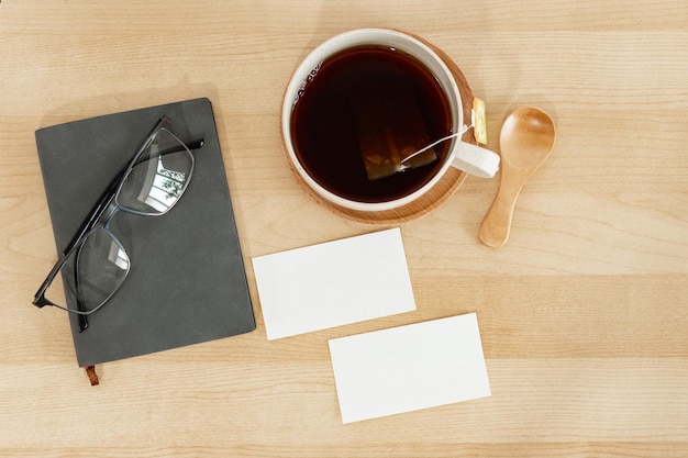 Gray notebook reading glasses business card and teacup on wooden office desk