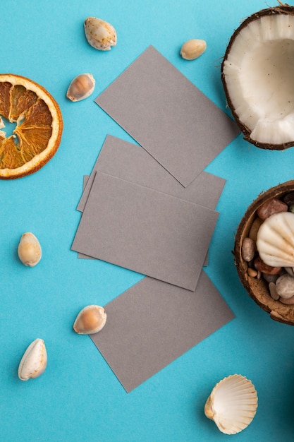 Gray paper business card with coconut and seashells on blue pastel background. Top view, flat lay, 