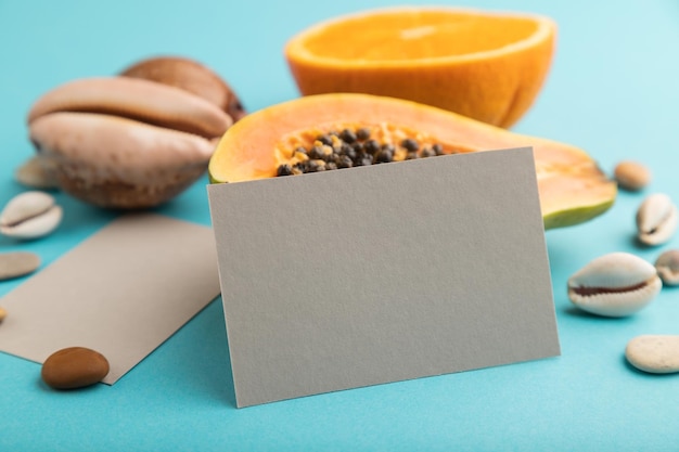 Gray paper business card with ripe cut papaya orange seashells on blue pastel pastel background Side view close up