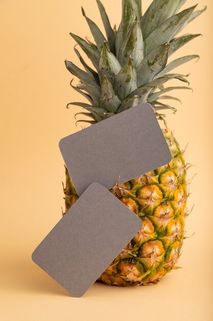 Gray paper business card with ripe pineapple on orange pastel background. Side view, copy space. 