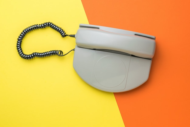 A gray retro phone on a two-tone orange and yellow background. Flat lay.