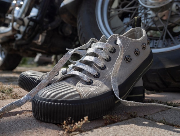 Sneakers grigie con teschi e lacci argentati e uno zaino nero in primo piano in piedi vicino al volante di