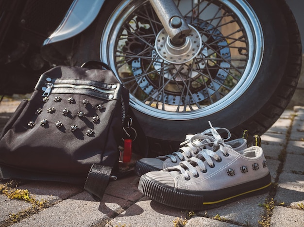 Gray sneakers with skulls and silver laces and a black backpack closeup standing near the wheel of