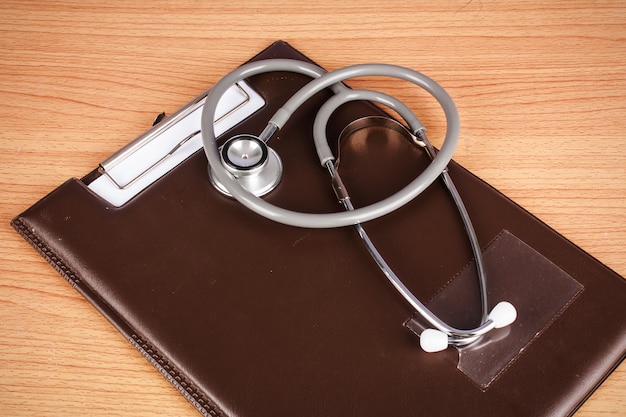 Gray stethoscope on brown clipboard wooden background