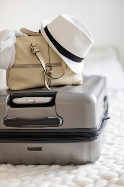 Gray suitcase with handbag and summer hat packing ready to travel vacation on bed at home or hotel