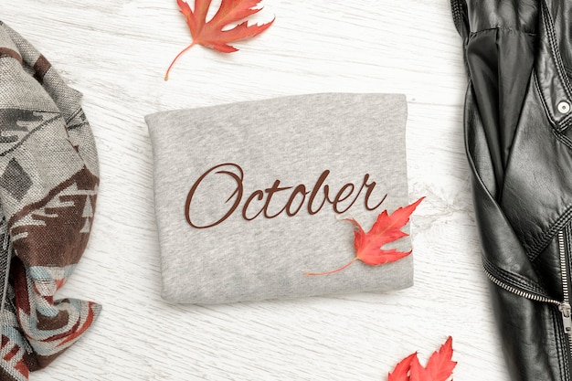 Gray sweater with inscription October, a black jacket, scarf and autumn leaves. Fashionable concept