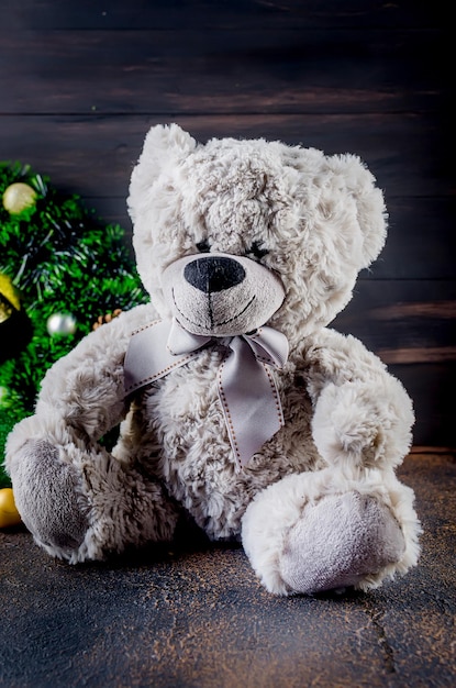 Серый плюшевый медведь в рождественской композиции с игрушкой в подарочной коробке и венком на темном фоне