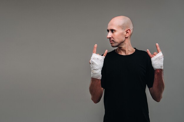 On a gray wall, a battered man in a black T-shirt With his hands wrapped up