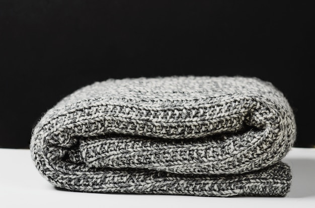 Gray wool knitted plaid, lies rolled up on white table.